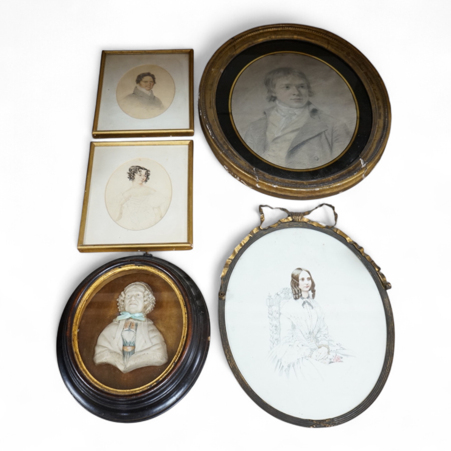 Four Regency and early Victorian portraits to include a pair of a lady and gentleman together with a carved wax bust of a lady wearing a bonnet, housed in an ebonised and gilt oval box frame, largest overall 38 x 32cm